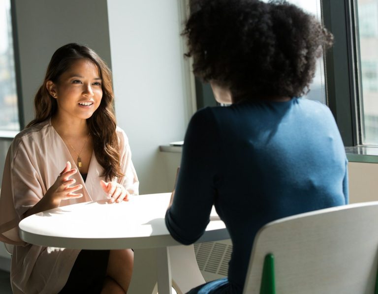 Deux femmes assises dans un espace moderne, discutant autour d'une table basse.
