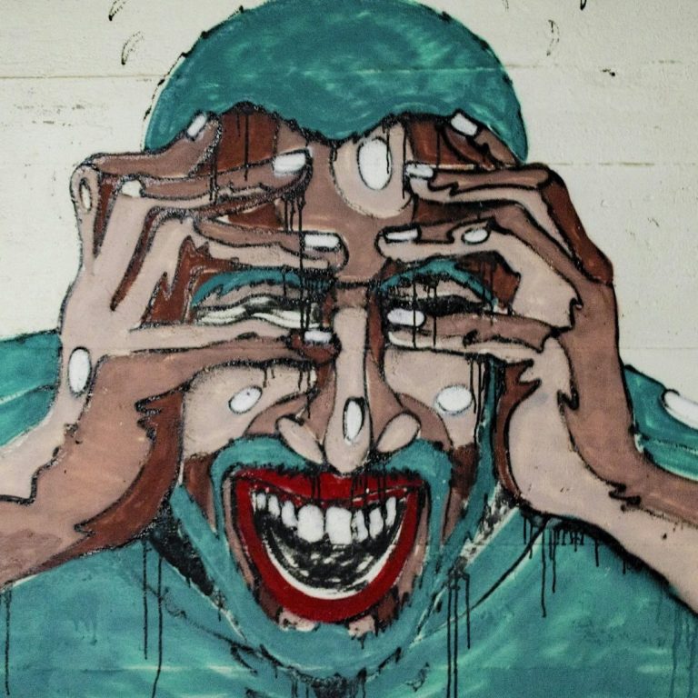 Conflit, médiation Un homme aux cheveux turquoise grimace, se tenant la tête avec des mains expressives.